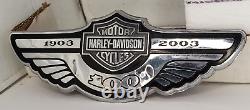 In French, the translation of the title 'Harley Davidson 100th Anniversary Fuel Gas Tank Badge Emblem-Silver Bar & Shield' would be:

'Insigne de réservoir d'essence commémoratif du 100e anniversaire Harley Davidson - Barre et bouclier argentés'