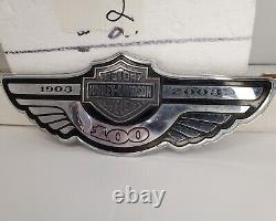 In French, the translation of the title 'Harley Davidson 100th Anniversary Fuel Gas Tank Badge Emblem-Silver Bar & Shield' would be:

'Insigne de réservoir d'essence commémoratif du 100e anniversaire Harley Davidson - Barre et bouclier argentés'